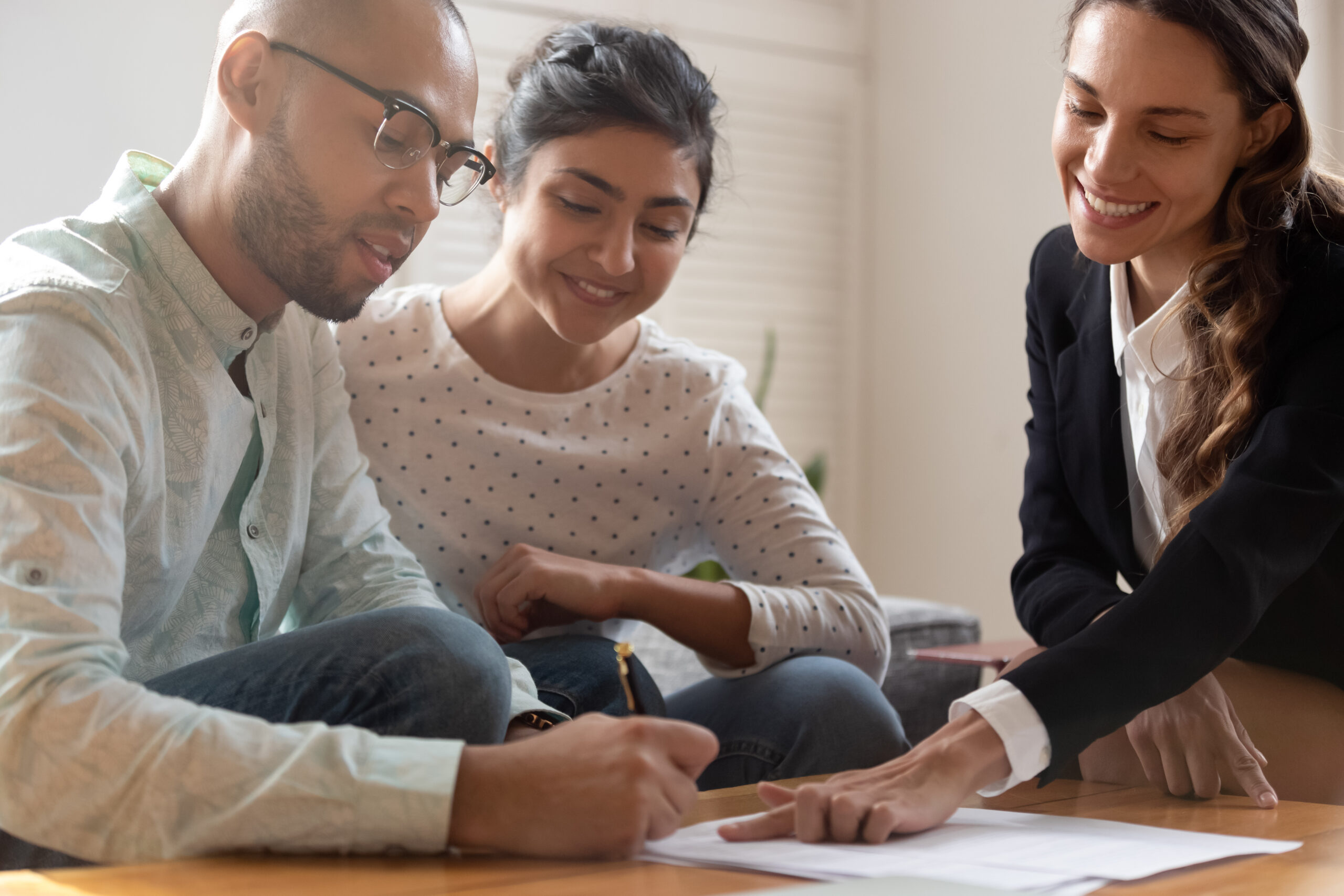 Happy Young Indian Woman Watching African American Husband Putting Signature on Agreement