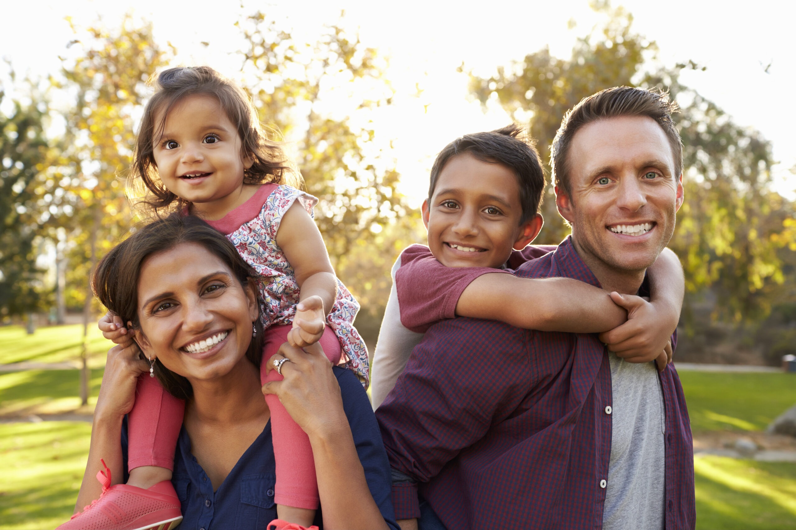 Mixed Race Parents Carry Their Kids Piggyback in a Park